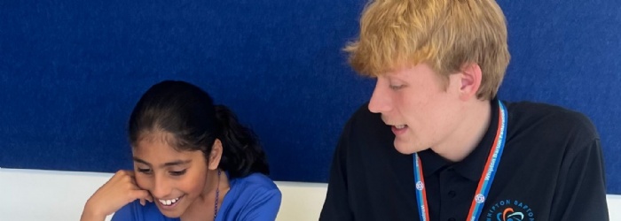 Member of staff from Whipton Barton Federation sat at a table teaching a pupil.